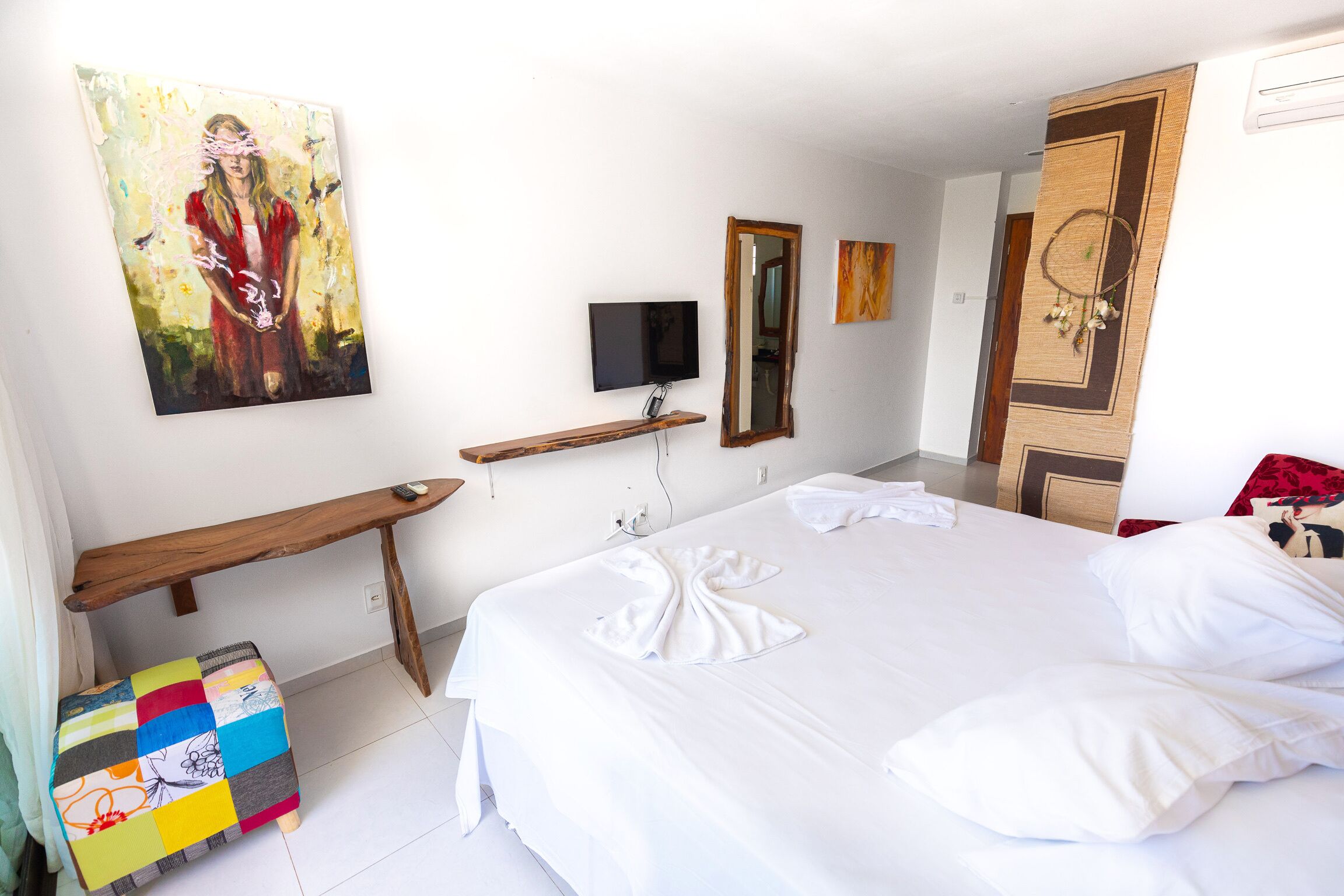 A hotel room with a bed, a TV, a painting, and a wooden bench.