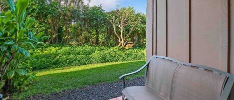 A patio with a bench, surrounded by a well-maintained garden and a view of a building.