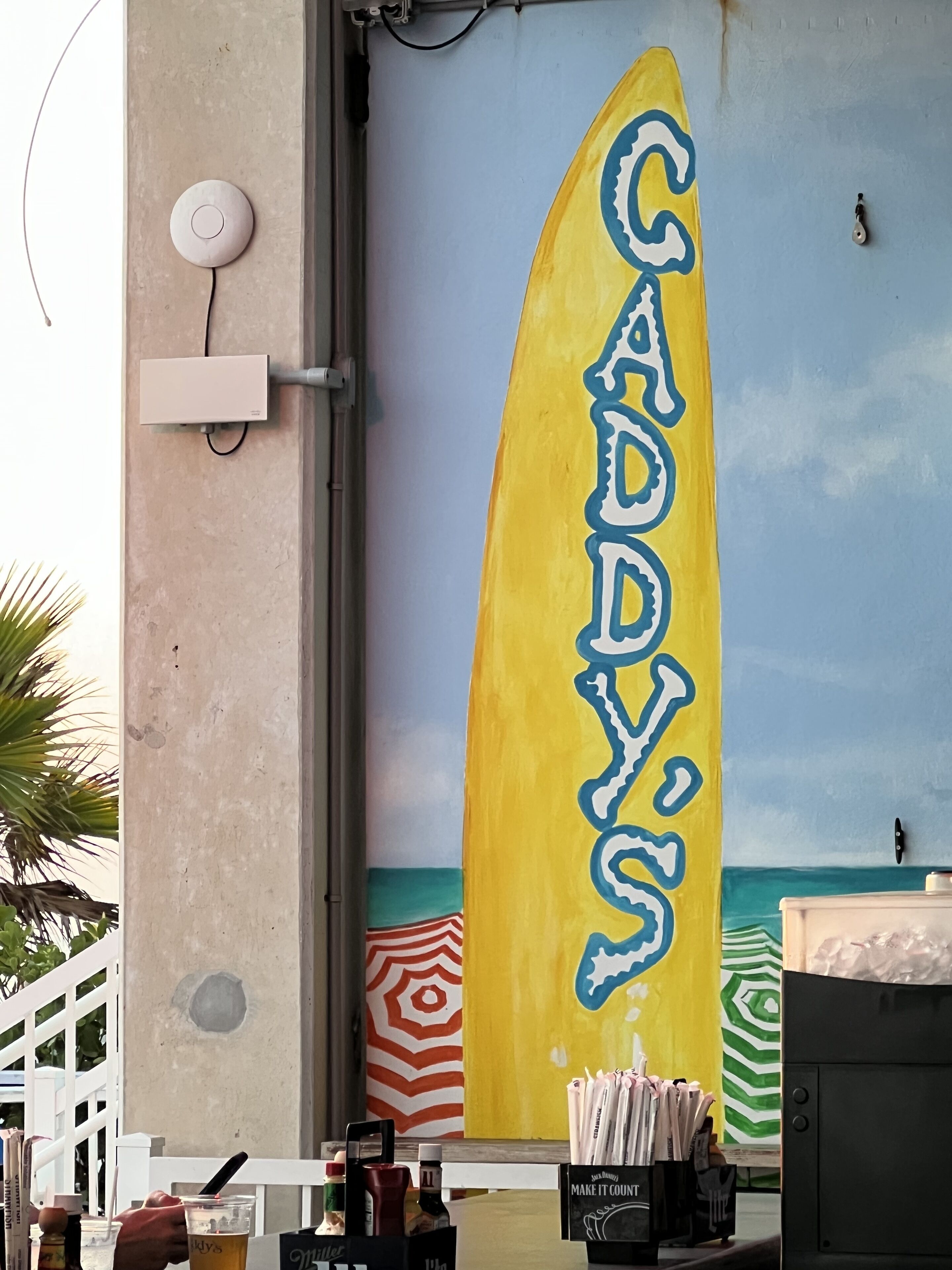A surfboard-shaped sign with the name 'CADDY'S' painted on it.