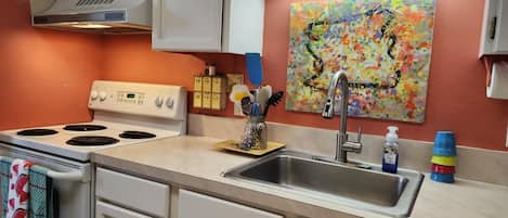 A kitchen with a stove, sink, and a colorful abstract painting on the wall.