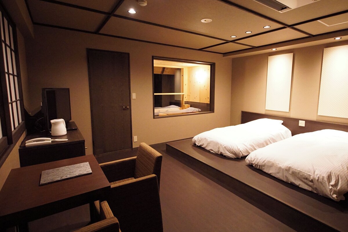 Une chambre d’hôtel avec deux lits, un bureau avec une chaise, une lampe de bureau, un téléphone et un miroir.