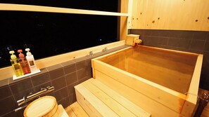 A wooden bathtub in a room with a window, a sink, and three bottles of soap on a shelf. - Atami Tsukiemon (Atami)