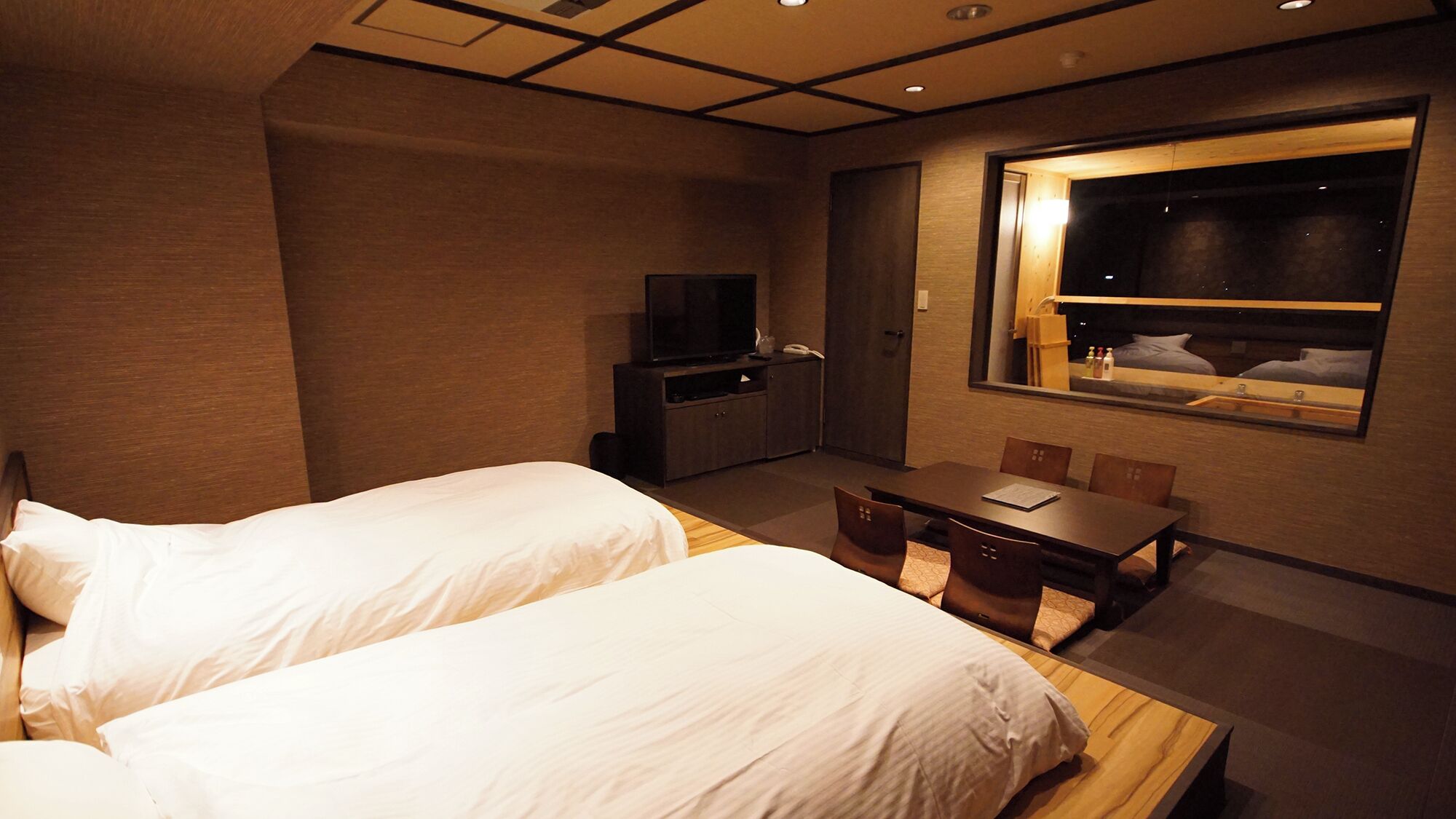 A hotel room with two beds, a desk, a television, and a window with a view.