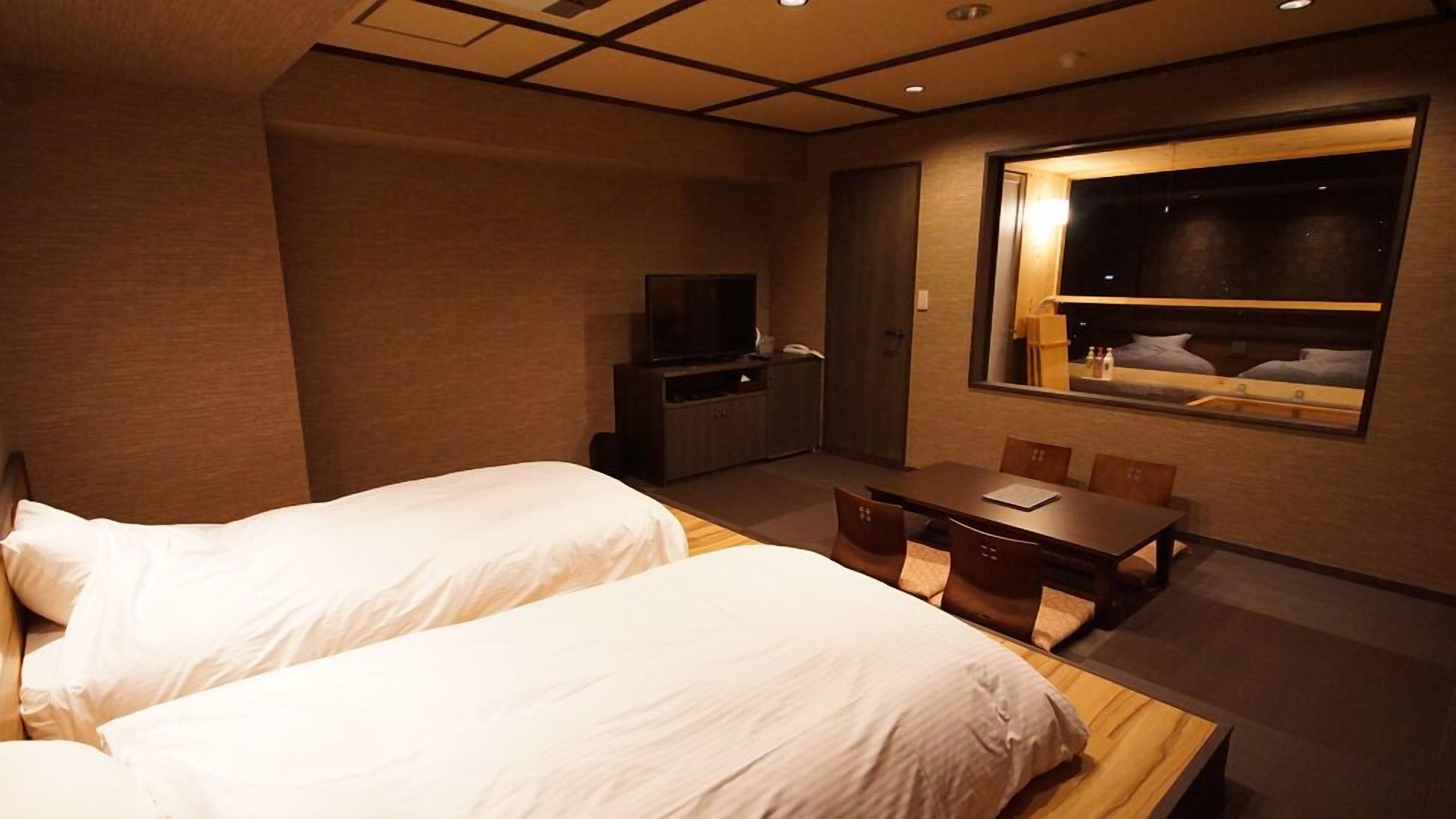 A hotel room with two beds, a desk, a television, and a window.
