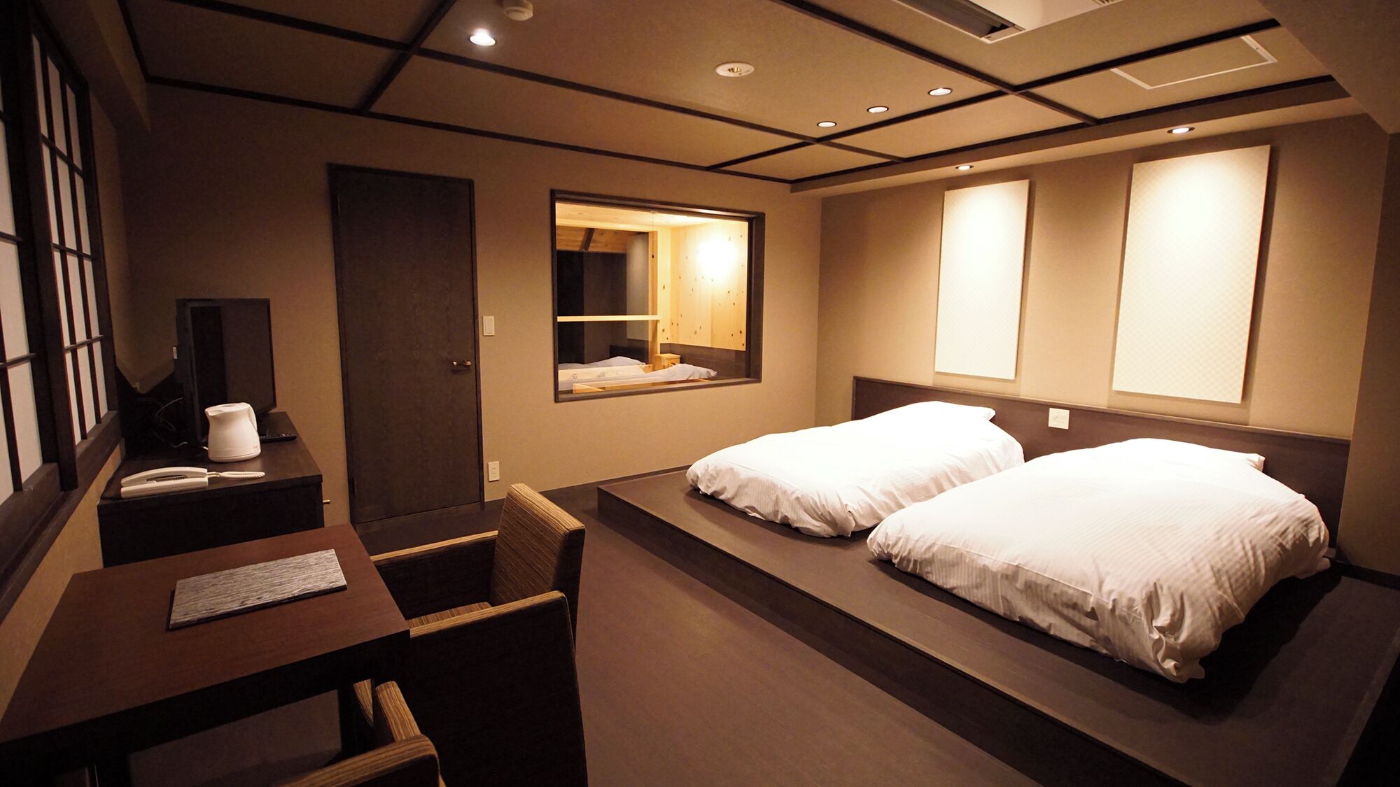 A hotel room with two beds, a desk with a chair, a desk lamp, a telephone, and a mirror.