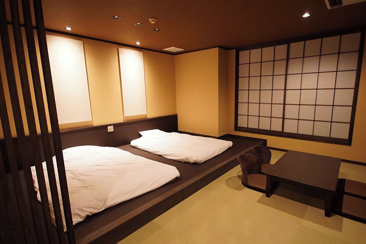 A room with two beds, a table, chairs, and a shoji screen.