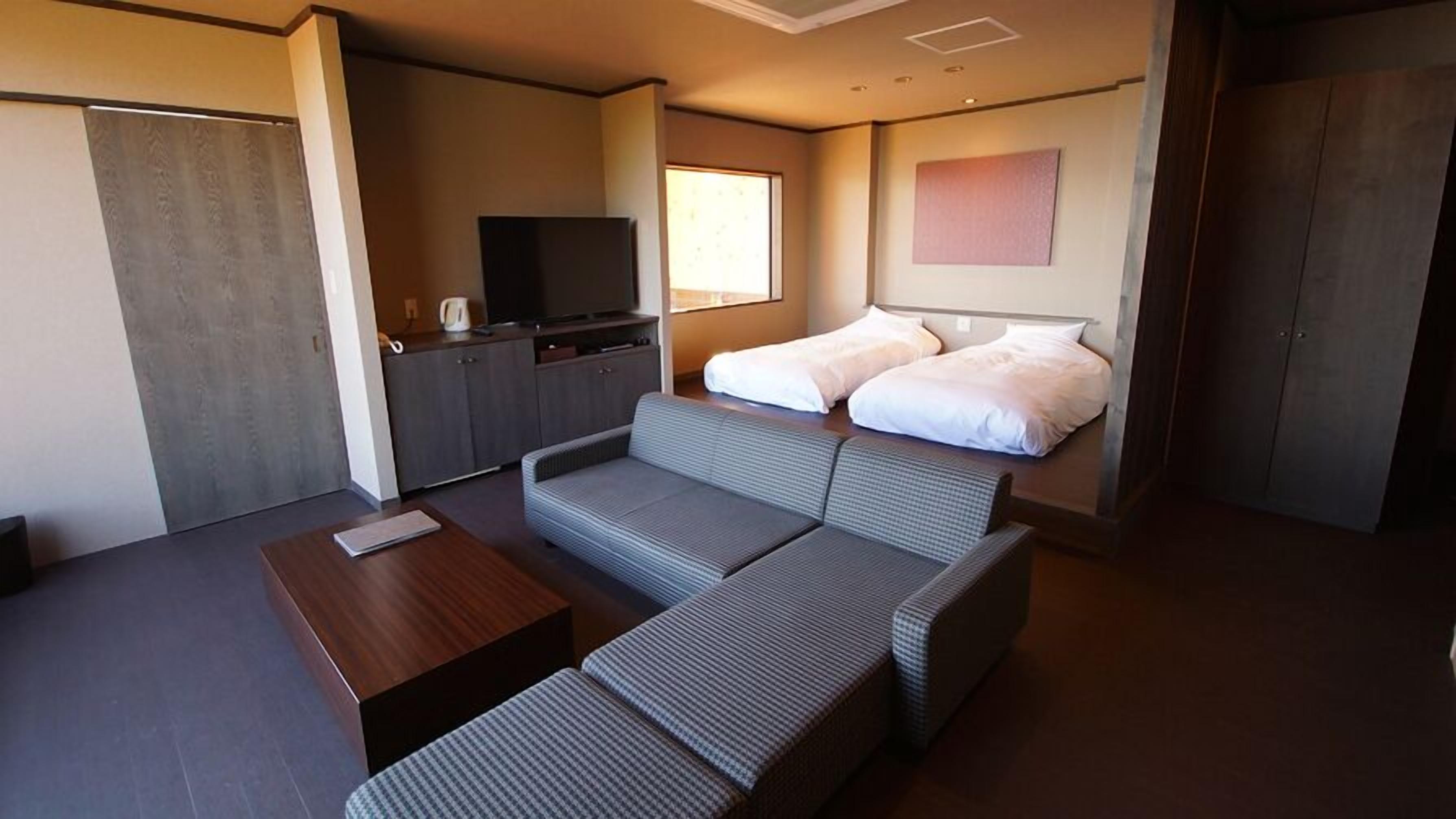 A modern hotel room with a sofa, a TV, a coffee maker, and a wardrobe.