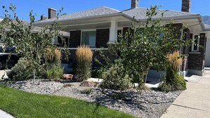 Ein modernes Haus mit Backsteinfassade, überdachter Veranda und einem angelegten Vorgarten mit verschiedenen Pflanzen und einem Kiesweg.