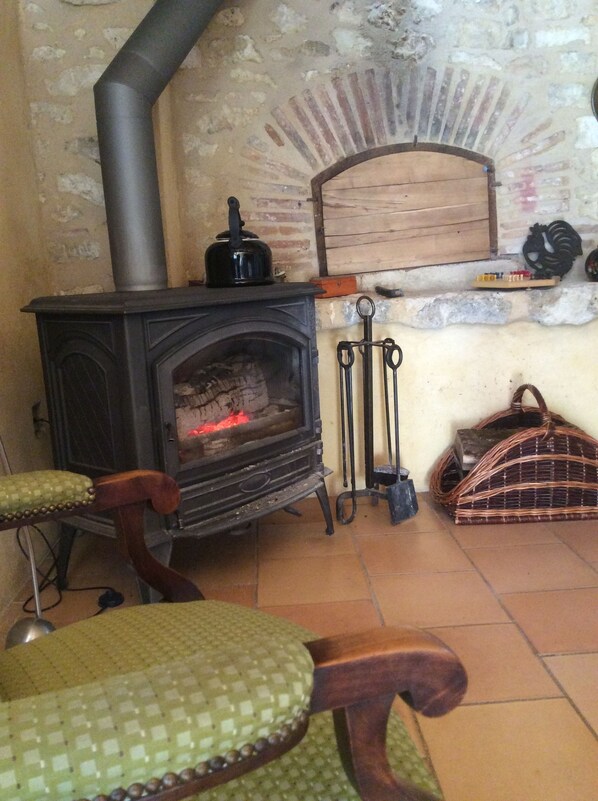 A rustic room with a wood-burning stove, a woven basket, and a wooden bench. - Le Clos Pastel (Virac)