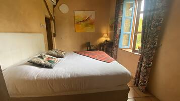 A bedroom with a bed, a desk, a chair, a window with curtains, and a wall-mounted air conditioner.