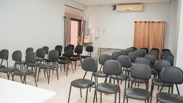 Una sala conferenze con file di sedie nere, un tavolo bianco e un condizionatore d'aria a parete.