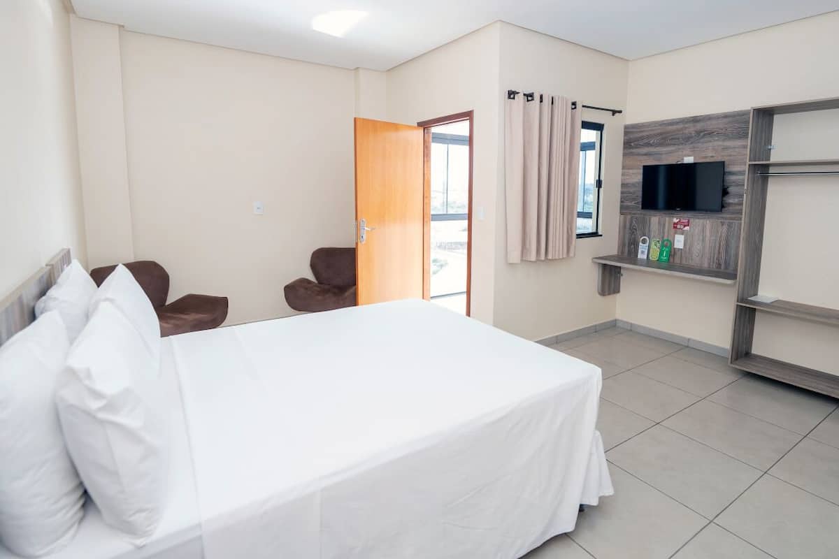 A hotel room with a bed, a TV mounted on the wall, a chair, and a door leading to a balcony.