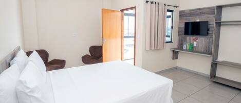 Habitación de hotel con cama, televisor montado en la pared, una silla y puerta que da a un balcón.
