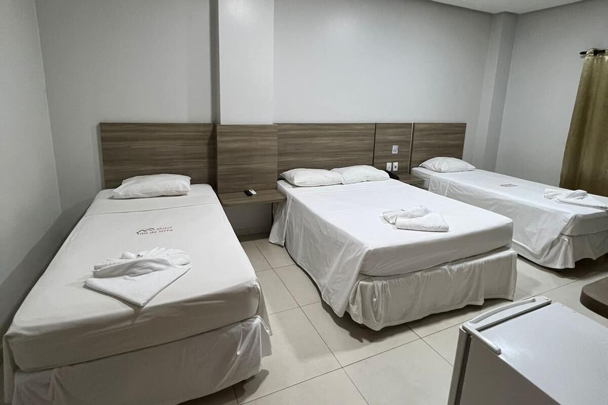 A hotel room with three single beds, a small refrigerator, and a bedside table with a lamp.