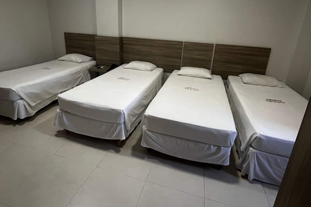 A hotel room with four single beds, each with a wooden headboard and white bedding.