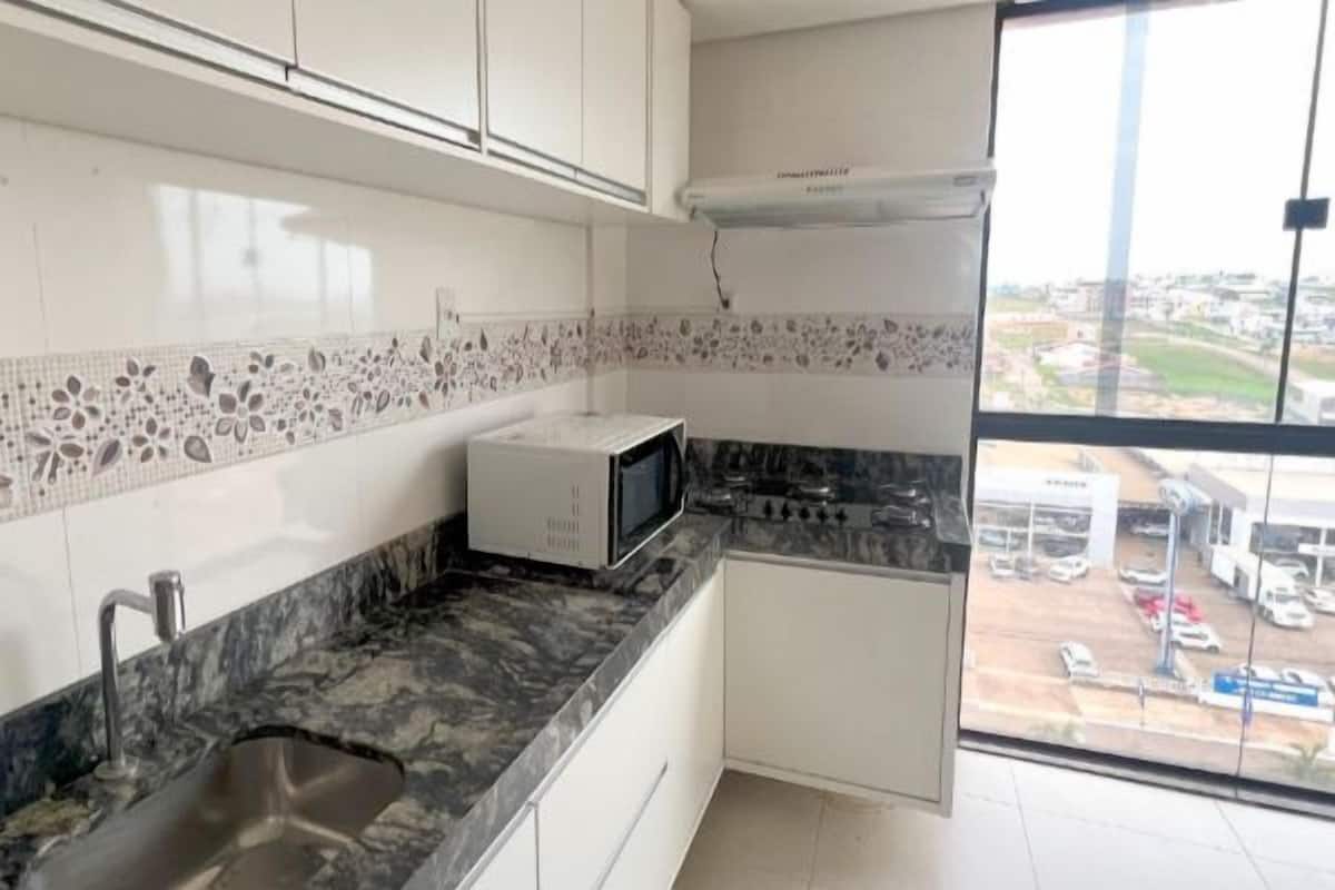 A kitchen with a microwave, stove, and sink. There is a window with a view of a parking lot and buildings.