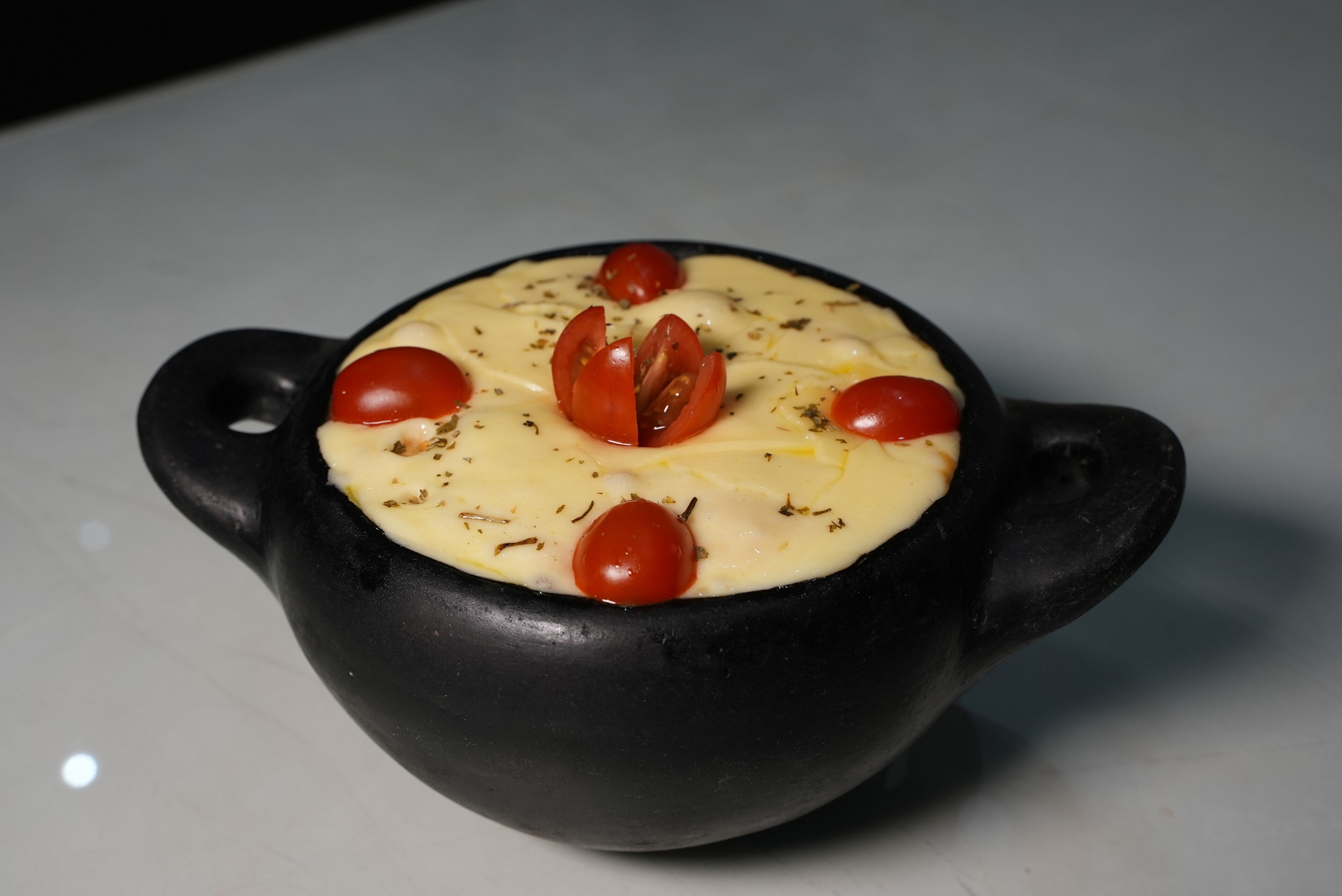 A black ceramic bowl with a creamy substance, garnished with cherry tomatoes and herbs.
