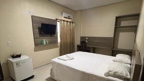 A hotel room with a bed, a TV mounted on the wall, a small refrigerator, and a bedside table with a remote control. - Hotel Vale Da Serra (Parauapebas)