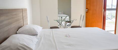 Habitación de hotel con cama, una mesita de vidrio y una puerta que da a un balcón.