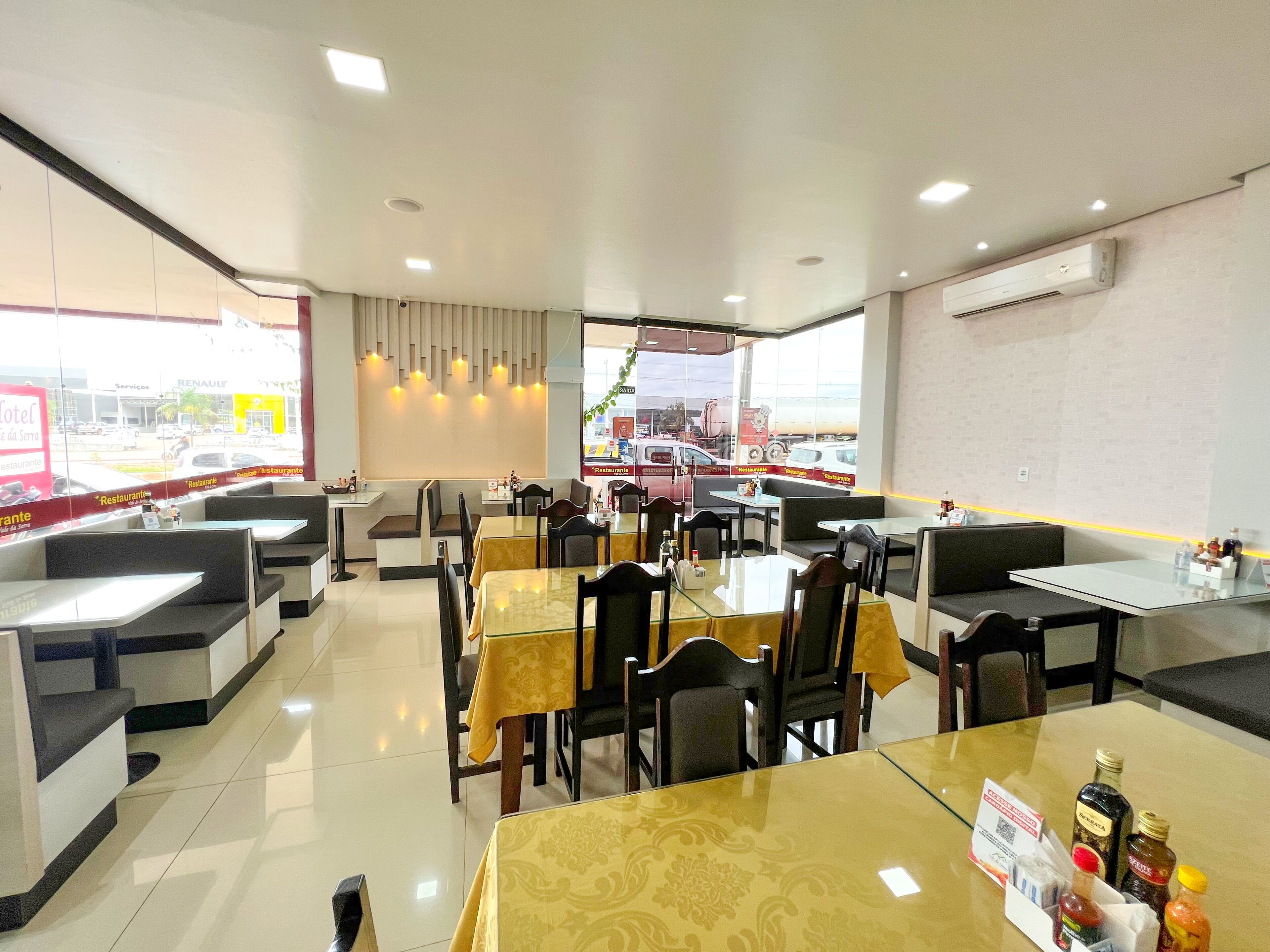 A modern restaurant with booths and tables, a view of the outside, and an air conditioning unit on the wall.