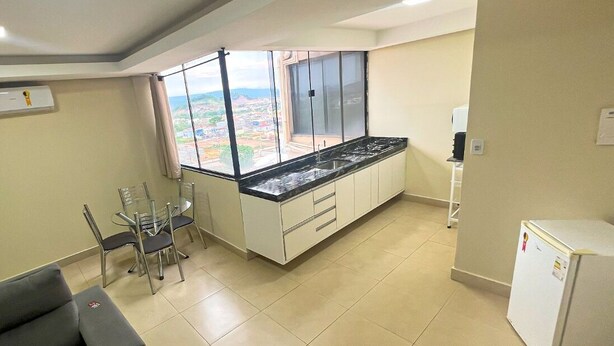 A compact kitchen with a large window, a dining area with chairs, and a refrigerator. - Hotel Vale Da Serra (Parauapebas)