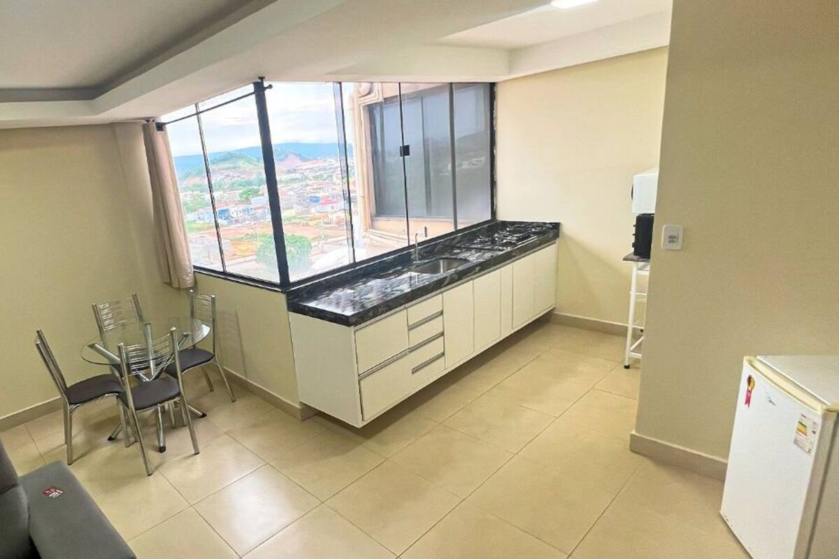 A compact kitchen with a large window, a dining area with chairs, and a refrigerator.