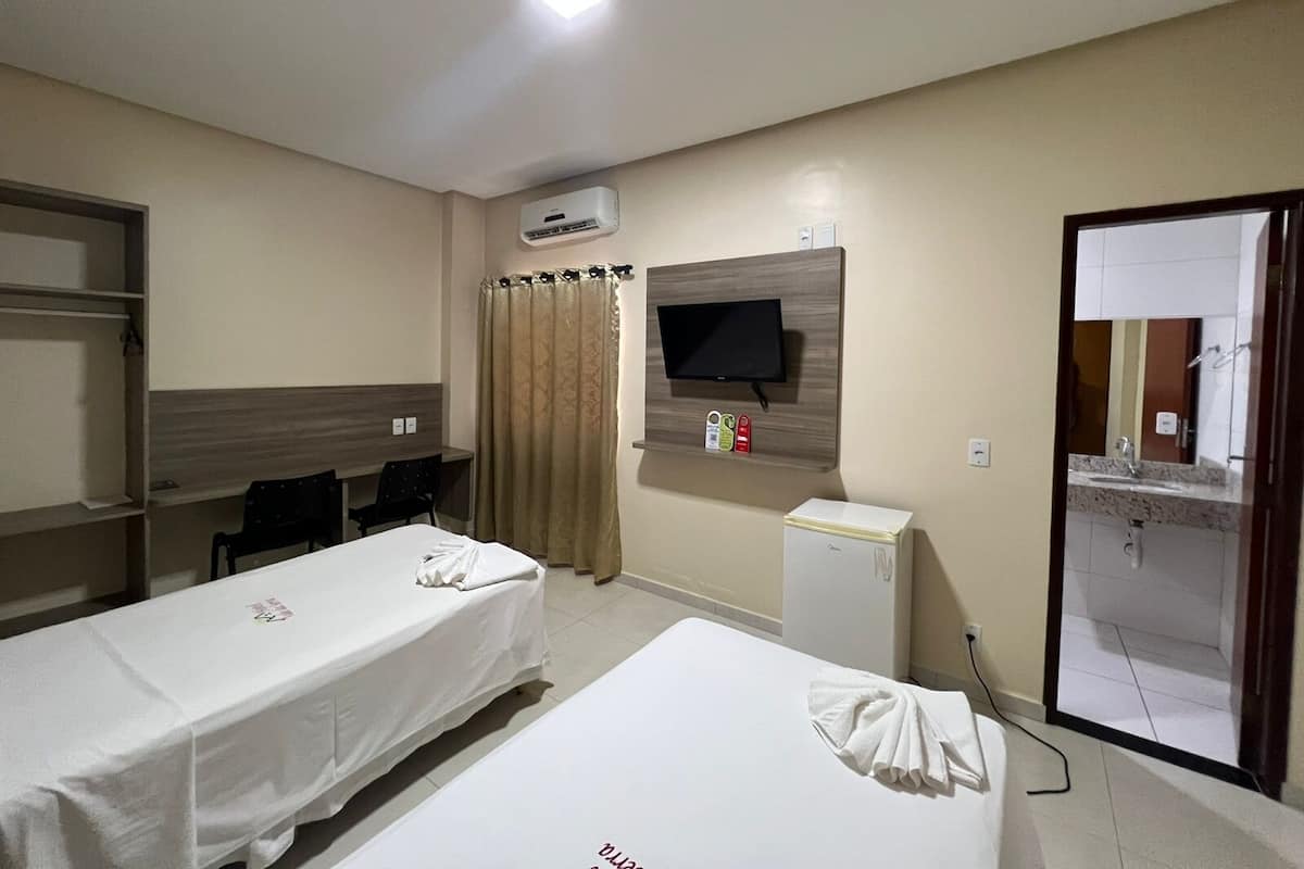 A hotel room with two single beds, a desk with a chair, a television mounted on the wall, and a small kitchenette.