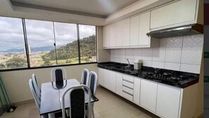 A kitchen with a dining table and chairs, white cabinets, a black countertop, and a view of a green landscape through large windows. - Hotel Vale Da Serra (Parauapebas)