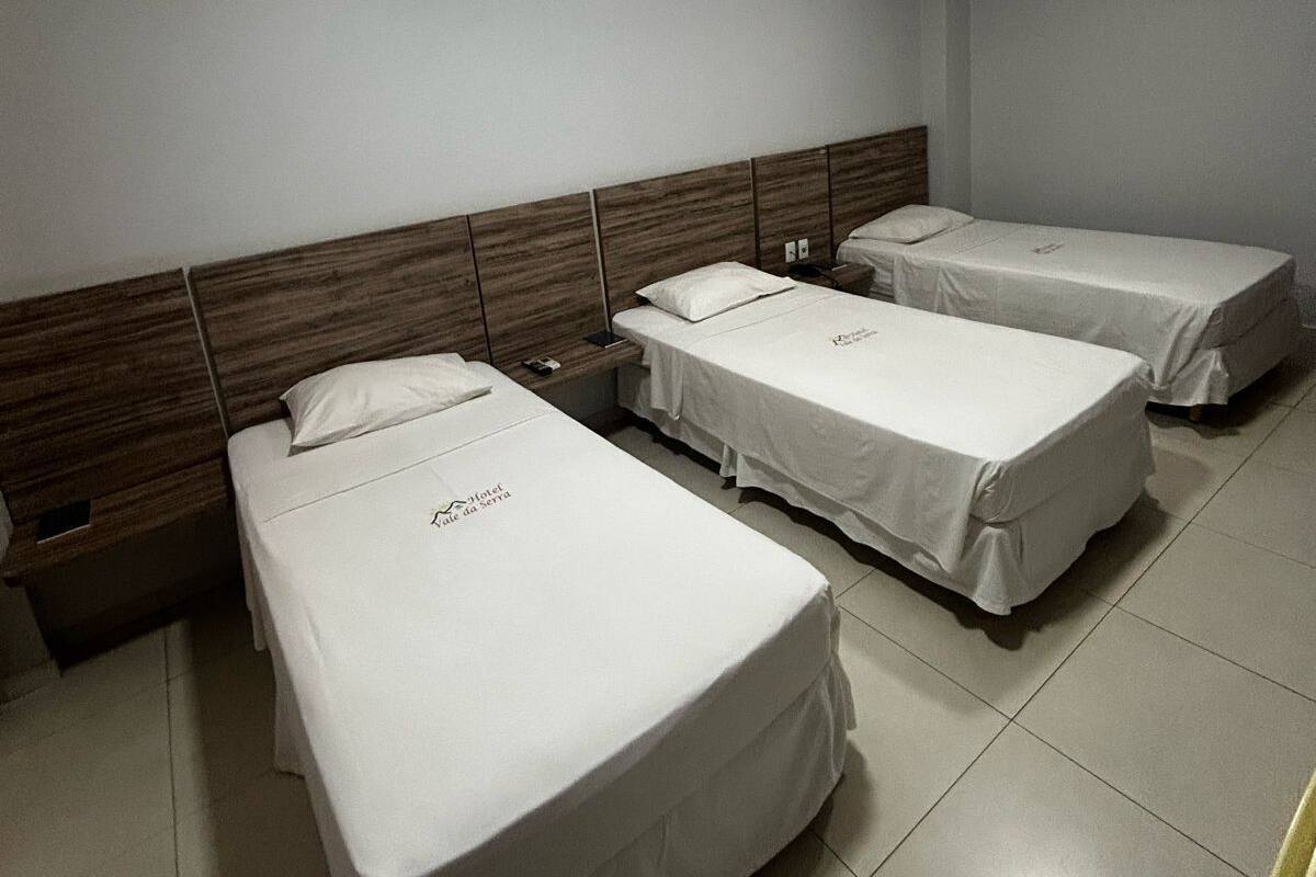 A hotel room with three single beds, each with a wooden headboard and white bedding.