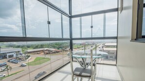 A high-rise hotel room with a large glass window offering a view of a cityscape, a glass table, and a modern chair. - Hotel Vale Da Serra (Parauapebas)