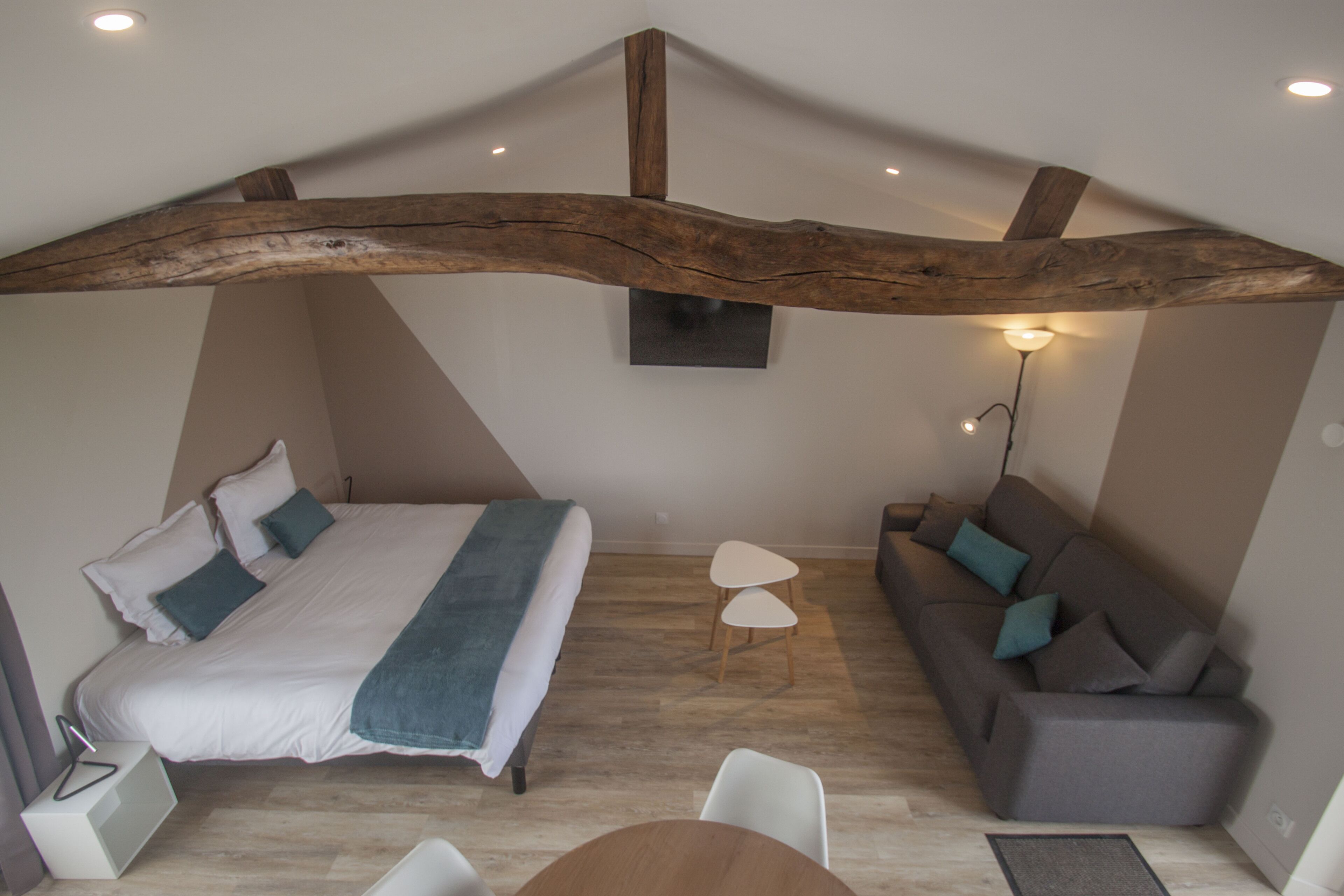 A bedroom with a large bed, a sofa, a small table, and a wooden beam ceiling.