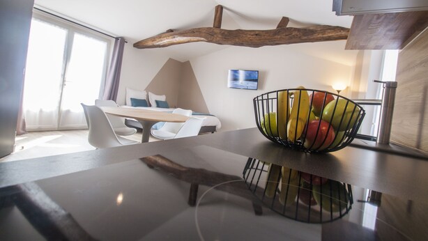 Una cocina moderna con techo de vigas de madera, un comedor con mobiliario blanco y un frutero en la encimera.