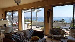A cozy living room with a sofa, a dining table, and a balcony with a view of the sea. - Holiday house facing the sea (Trébeurden)