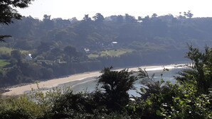 A coastal landscape with a beach, forested hills, and a few buildings in the distance. - Holiday house facing the sea (Trébeurden)