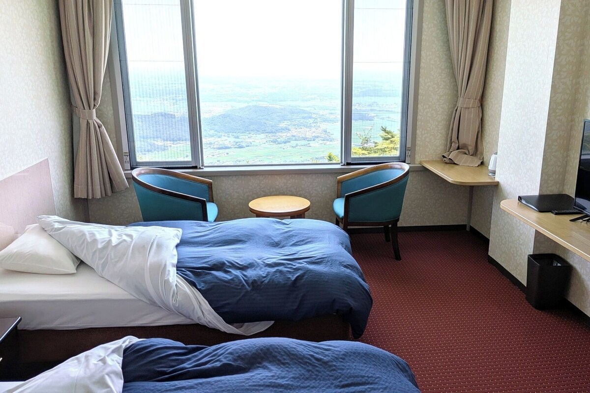 Habitación de hotel con dos camas, televisión, una mesita y ventana con vistas.