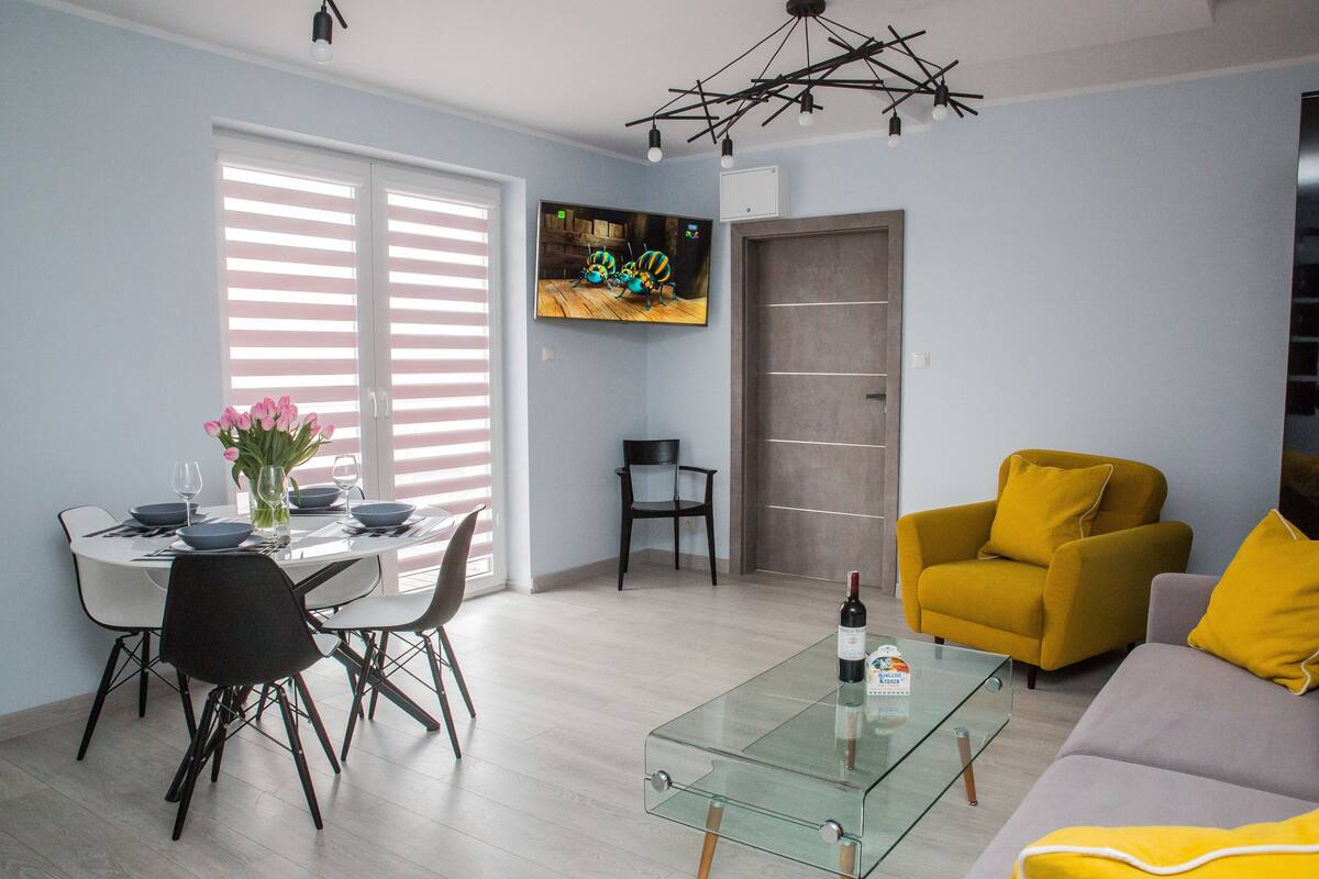 Ein modernes Wohnzimmer mit einem Glastisch, einer Couch und einem Essbereich mit Stühlen und einem Tisch für zwei Personen.