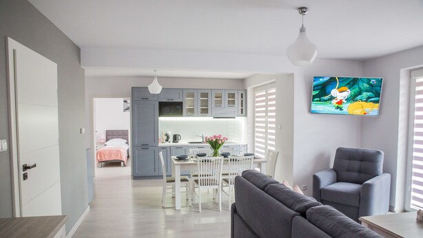 A modern living room with a grey sofa, a grey armchair, and a dining area with a white table and chairs. - Apart Harmony (Wladyslawowo)