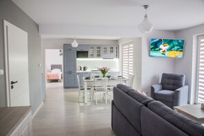 A modern living room with a grey sofa, a grey armchair, and a dining area with a white table and chairs. - Apart Harmony (Wladyslawowo)