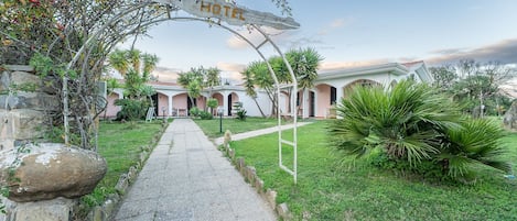 A hotel entrance with a pathway leading to a building with multiple arches and a sign that reads "HOTEL".