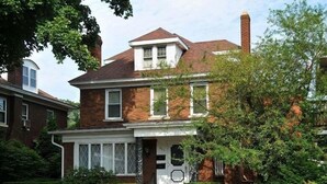 A two-story brick house with a front porch, a chimney, and a well-maintained garden.