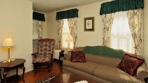 A living room with a patterned sofa, a floral chair, and a table with a lamp.