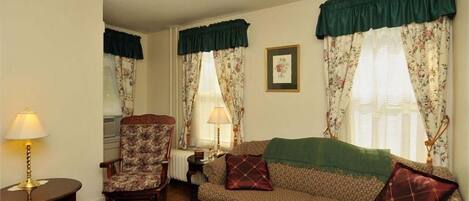 Una sala de estar con un sofá estampado, un sillón floral y una mesa con lámpara.
