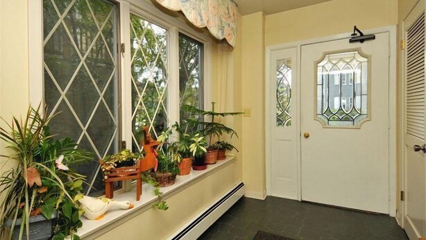 A hallway with a window seat lined with potted plants and a door with a stained glass design.