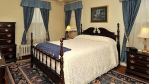 A bedroom with a four-poster bed, a chandelier, a painting on the wall, and a patterned rug.