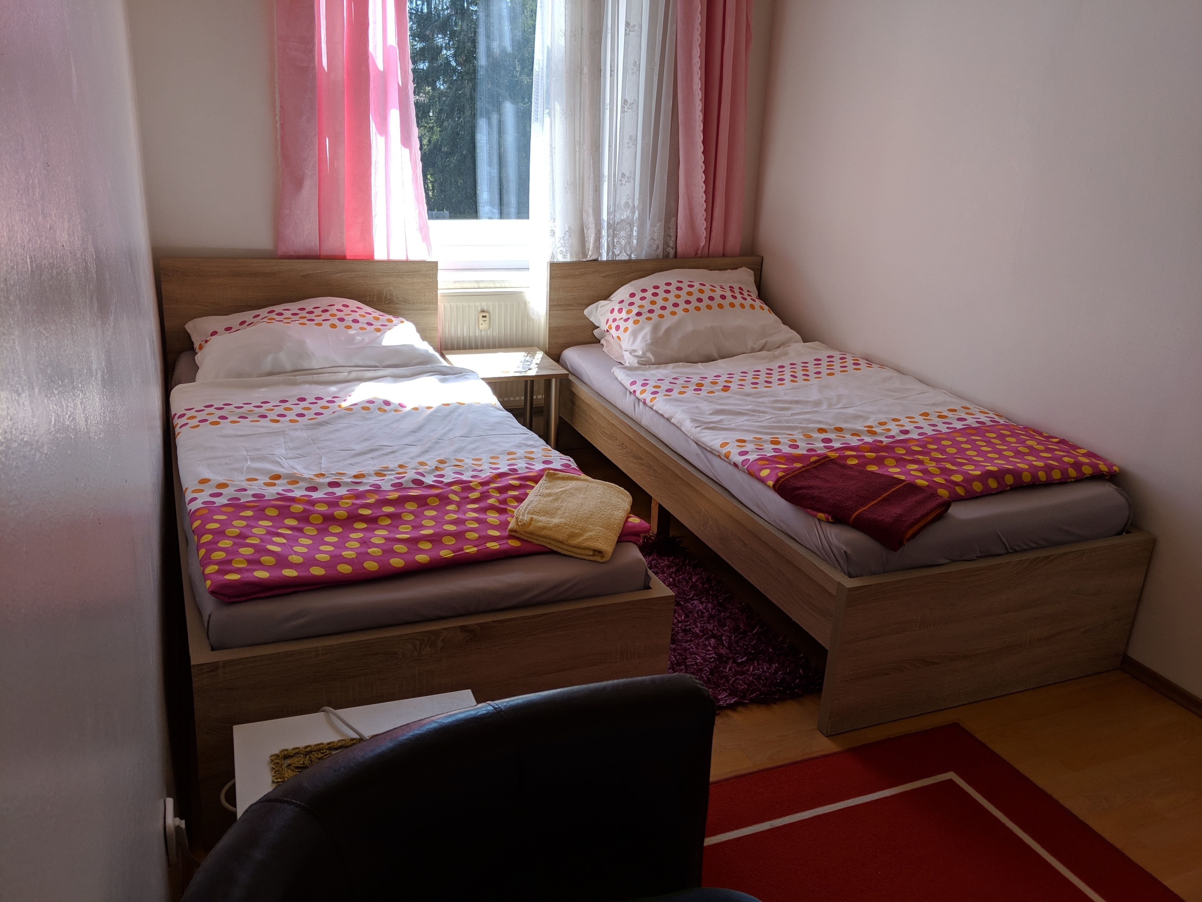 Una habitación pequeña y acogedora con dos camas individuales, cabecero de madera, una mesita y una silla.