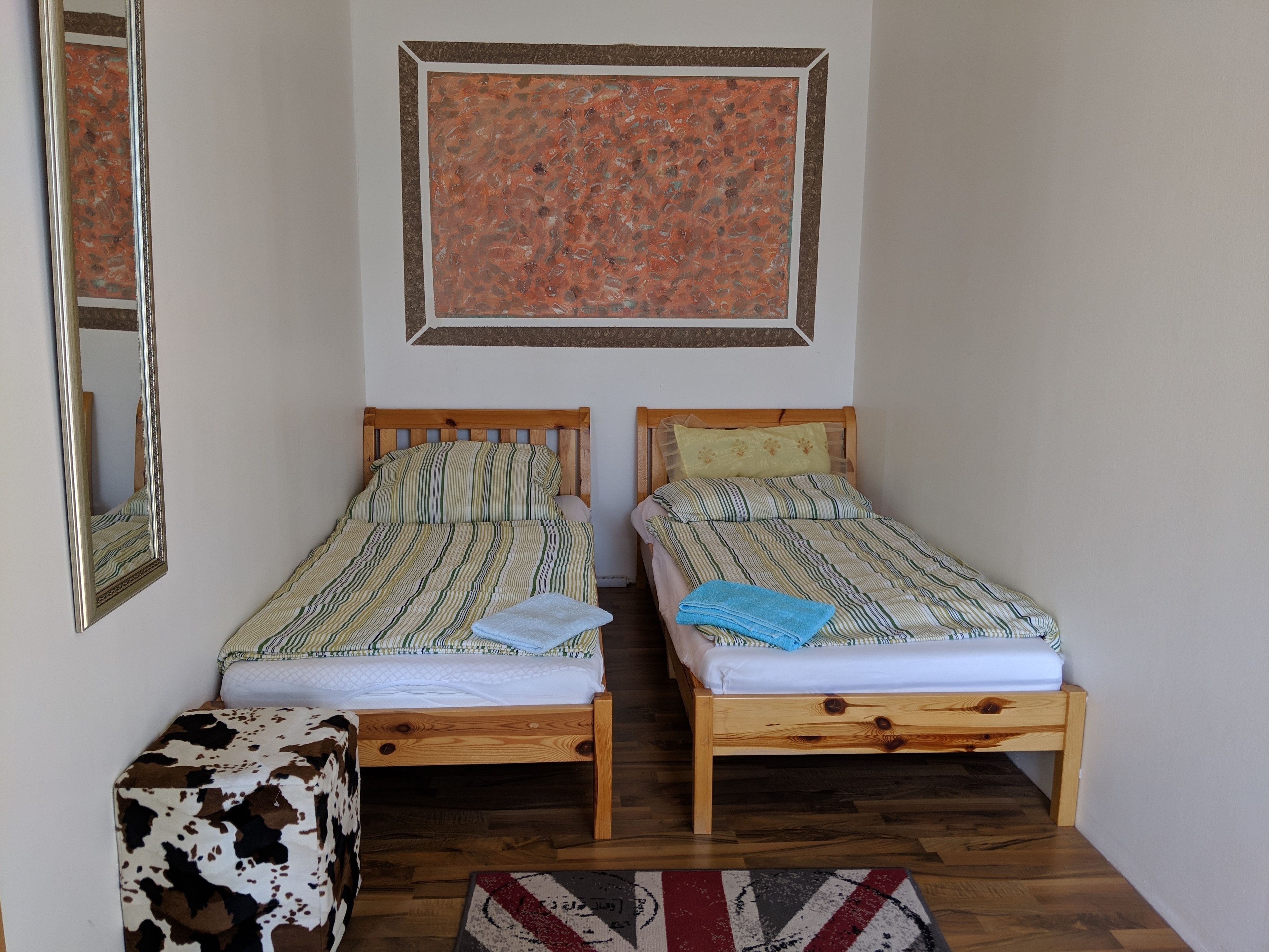 A room with two wooden beds, a mirror, a cow-patterned ottoman, and a rug.