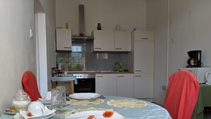 Un comedor con una mesa preparada para dos, una cocina al fondo y una cafetera sobre una encimera.
