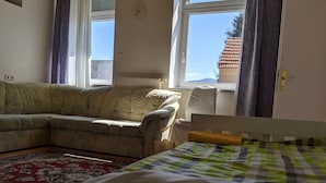 Una habitación con sofá, cama, ventana con cortinas y vistas a un edificio.