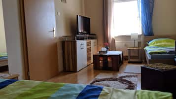 Un dormitorio con una cama, un escritorio con computadora, televisión y una ventana con cortinas.