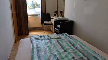 A bedroom with a bed, a chair, a dresser, a mirror, and a window with a view of the outside.